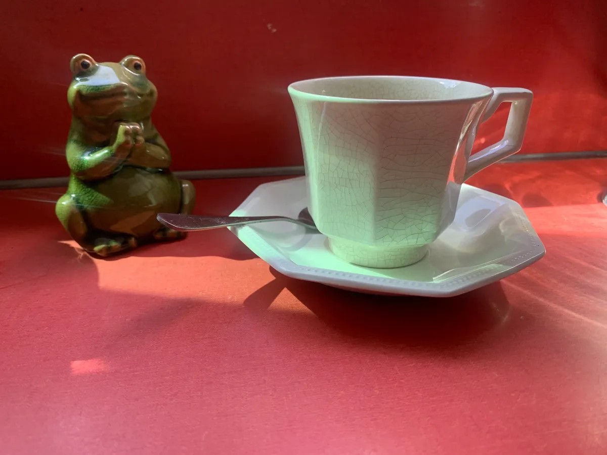 A ceramic frog beside a crackle-glaze teacup, on a red tabletop